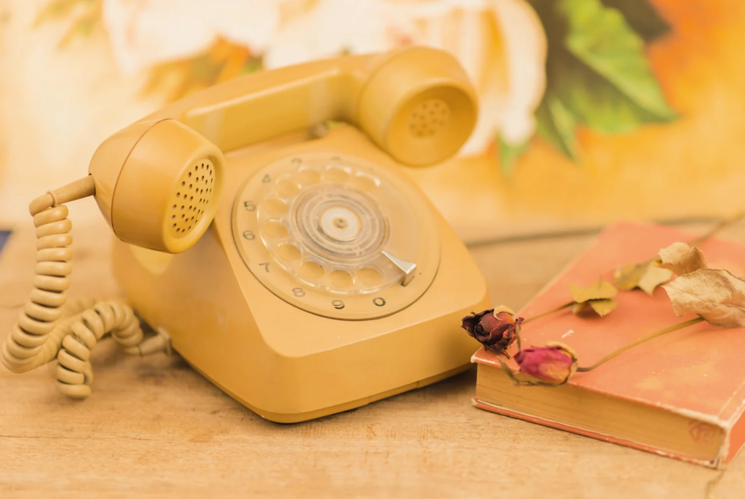 Téléphone à cadran vintage posé sur un bureau, avec un livre et une rose séchée